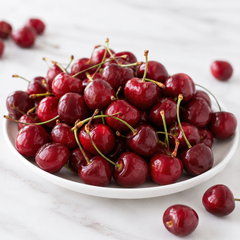 White plate with a pile of red cherries on a light wooden surface.