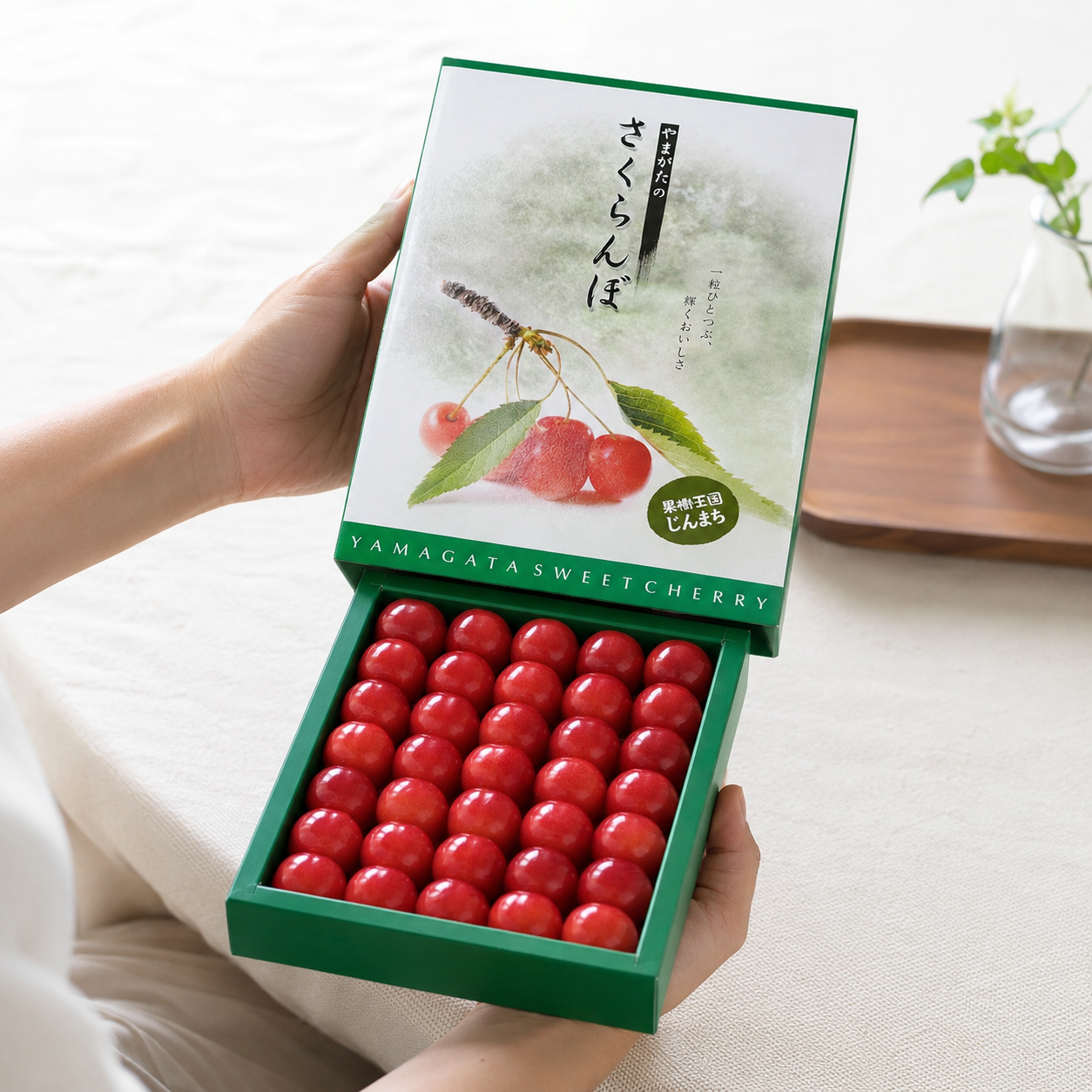 Hand holding a box of Yamagata sweet cherries with a green lid featuring cherry illustrations.