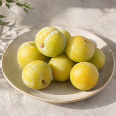 Whole and halved Emerald Beaut Plum featuring golden-yellow juicy flesh, smooth green skin, and naturally sweet California-grown fruit.