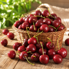 Basket of cherries on a wooden surface with a blurred green plant in the background