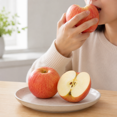 Person eating an apple with a plate of apples on a table