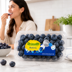 Driscoll's blueberries in a clear container with a woman eating blueberries in the background.