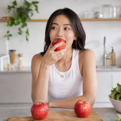 Woman eating an apple in a kitchen with envy apples on a cutting board in Singapore.