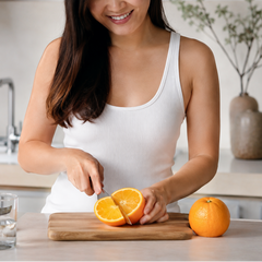 Woman cutting an orange on a wooden cutting board in a kitchen for juicing. 