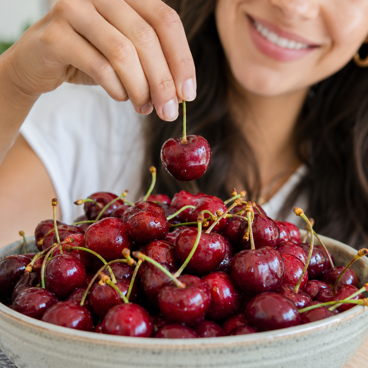 Person picking a cherry from a bowl of red fresh cherries