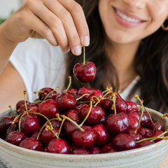 Person picking a cherry from a bowl of red fresh cherries