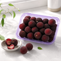 Container of red berries on a light surface with a plant in the background imported from SKC Fruits