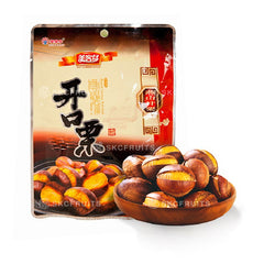 Packaged roasted chestnuts displayed alongside a wooden bowl of chestnuts, with a label in the background.